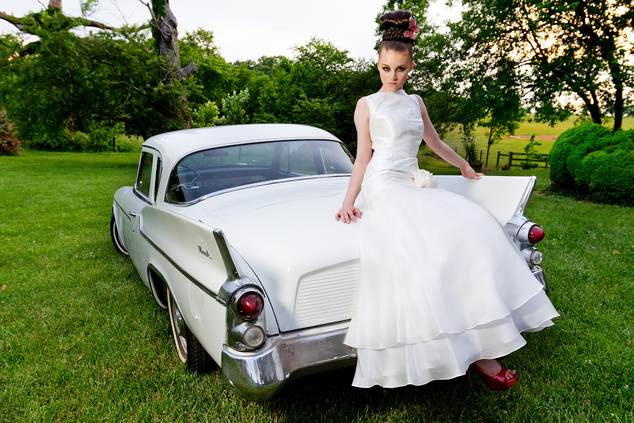 Bride in a white gown seated on a vintage car